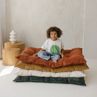 Child sitting on a stack of colorful tufted mattresses in a minimalistic room.
