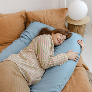 Woman lying on a large U-shaped body pillow on a couch in a cozy living room.