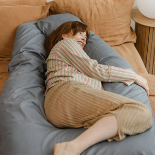 Expecting mother hugging the soft, stone grey MINICAMP U-shaped pregnancy pillow for back and belly support.