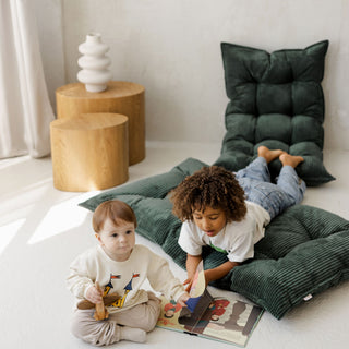 Two children sitting on green cushions reading a book in a cozy room.